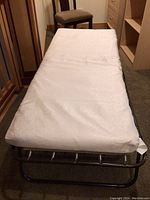 Single cot fully extended with mattress on top, showing metal tubular black frame and white mattress.