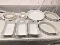 Overall view of the lot showing various white ceramic bakeware including oval dishes, rectangular trays, small bowls and patterned Corningware dish.