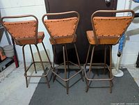 Rear view of three vintage orange swivel bar stools showing backrest design and metal frame.
