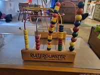Front view of wooden bead rollercoaster toy with colorful wooden beads on metal wires and wooden base.