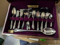 Photo of the interior of the wooden storage box with multiple slots of cutlery pieces laid horizontally and several spoons and forks visible within velvet-lined compartments.