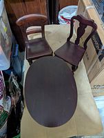 Oval wooden doll table and two wooden doll chairs viewed from above, showing dark finish of furniture surfaces.