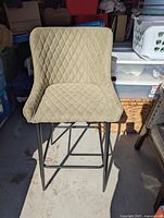 Front-facing view of green bar stool showing diamond-quilted upholstery and black metal legs.
