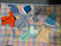 Top-down view of seven hand-made doll clothes for Barbie dolls laid out on checkered fabric.