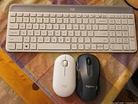 White Logitech wireless keyboard with numeric keypad and two Logitech wireless mice (white and black) on a cloth surface.