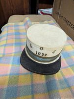 Front angle view of vintage Loyal Orange Lodge hat showing the cap top, front visor, and LOL 1022 inscription, placed on a pastel plaid fabric.