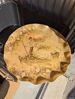 Top view of large circular serving platter showing the fishing man illustration and scalloped edges.