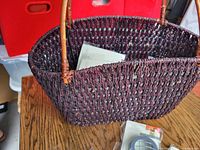 Purple rectangular wicker basket with wooden handle placed on a wooden surface, showing woven texture and open top.