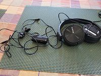 Sony wired in-ear earbuds with inline noise cancelling controller and black wired over-ear headphones with one missing ear cup end plate shown on a green woven placemat.