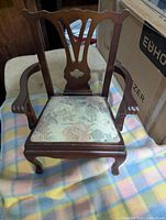 Front view of the wooden doll chair showing carved backrest detail and upholstered seat.