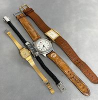 Four vintage wrist watches laid out on gray surface showing straps and faces.