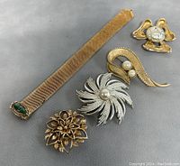 Lot contents showing all five jewelry pieces: four brooches and one mesh bracelet on a dark gray surface