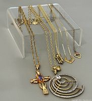 Photo showing five necklaces displayed on a clear stand, highlighting chain lengths and pendant designs including the cross and circular pendants.