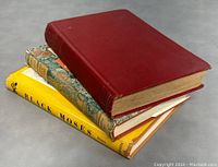 Three stacked antique books: a red hardcover book on top, a marbled hardcover book in the middle, and 'Black Moses The Real Uncle Tom' with a yellow dust jacket on the bottom.