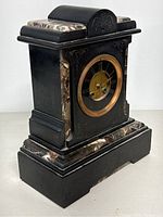 Side and partial front view of antique marble mantel clock showing black marble body with decorative brown and white marble insets and gold bezel around clock face.