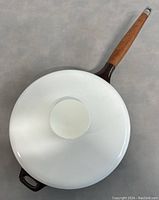 Top view of white enamel coated lid of cast iron pan with wooden handle.