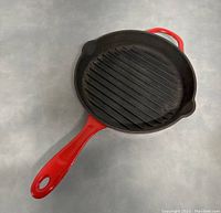 Top view showing black ridged cooking surface and red handle with hanging hole.