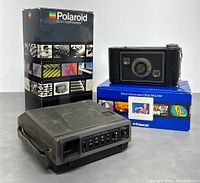 Polaroid 35mm AutoProcessor, Polaroid 35mm Illuminated Slide Mounter with slide shown, and vintage Kodak film camera grouped together with original boxes for processing and mounting units.