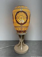 Front view of the lit porcelain table lamp showing intricate pierced lattice and floral wreath pattern.
