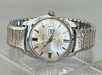 Front angle view of Helbros wristwatch with silver dial, day and date windows, and expandable metal strap.