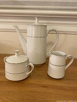 Full 3-piece coffee set including coffee pot, creamer, and sugar bowl on wooden surface against wall.