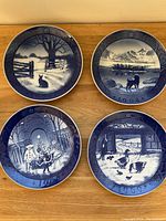 Four Royal Copenhagen plates laid out on a wooden surface showing all seasonal and scenic designs.