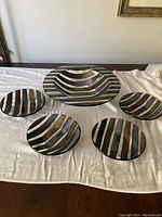 Full view of the 5 piece fused glass salad set laid out on a table. Includes one large serving bowl and four smaller individual bowls with striped designs in metallic and iridescent tones.