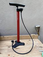 Full view of the Bontrager Turbo Charger HP bike pump standing on wooden surface showing handle, red body, hose and black base.
