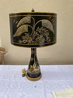 Full view of vintage black lamp with golden and beige hand painted floral patterns on both shade and base. Cord visible to the side.