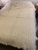 Full view of cream wool throw spread out on double bed, showing the size and cable knit pattern.