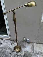 Full view of the brass finished metal floor lamp showing adjustable arm, round base, and overall height
