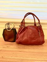 Red leather Fossil purse and brown Brighton purse side by side on wooden surface