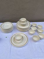 Overview of entire set arranged on a table showing dinner plates, bowls, cups, and saucers in ivory color with gold/beige trim.