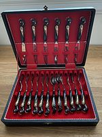 Open black box showing all 18 pieces: 6 knives on top slot, 12 forks and spoons below, set in red velvet interior.