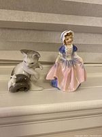 Two figurines side by side: Lladro kitten and mouse next to Royal Doulton girl in bonnet and dress.