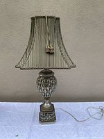 Full view of the lamp showing metal base with openwork design and striped shade with tassels