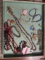 Photo of a collection of mixed costume jewelry including multiple necklaces, bracelets, earrings, a brooch, and a ring, displayed in a green tray.