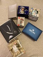 Photo shows mixed lot of boxed items including a gentlemen’s watch set, wine aerator, Bella & Rose box, floral cup set, and decorative wax sachet on a beige surface.