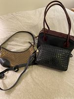 Three purses displayed on a beige surface, colors black, burgundy, gold, and black, different shapes and sizes.