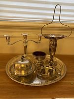 Photo showing the full set on wooden surface with window background, highlighting the silverplate tray, covered butter keeper, three arm candleholder, ruby glass liner, flower basket and compote