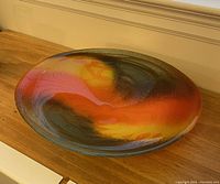 Angled side view showing the shallow, wide shape and colorful abstract design of the art glass bowl.