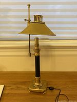 Full view of vintage brass candlestick lamp with black column and brass adjustable shade in front of window blinds