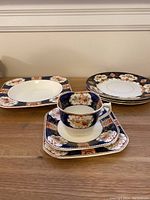 Overall view of the set including various plates, a teacup, and square dish showing cobalt blue backgrounds with floral and gold accents