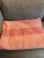Folded peach and coral pink wool blanket on a chair, showing texture and banded color design.