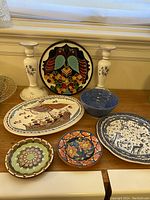 Seven pottery items including plates, candle holders, and bowl arranged on a table