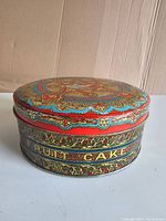 Photo showing the round decorative metal fruit cake tin with colorful patterns and inscriptions.