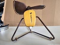 Side view of the Mid Century Modern electric fan showing the yellow motor housing with Elektromion branding and three brown blades on a triangular metal base.