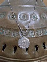 Photo showing sterling silver chain and round Gemini pendant on a textured floral metal surface.