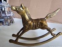 Side view of vintage brass rocking horse figurine showing horse profile, saddle, mane, tail and rocker curved bases
