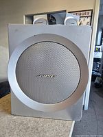Front view of large Bose subwoofer with silver circular grill and Bose logo.